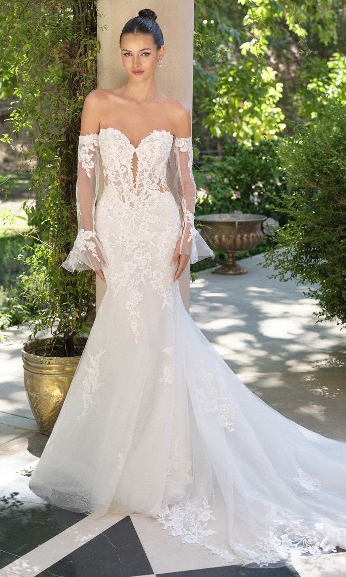 A woman stands outdoors in the Andrea and Leo WL065 long wedding dress, featuring a mermaid silhouette, sheer detachable lace sleeves, an off-the-shoulder lace bodice, and a flared tulle skirt.
